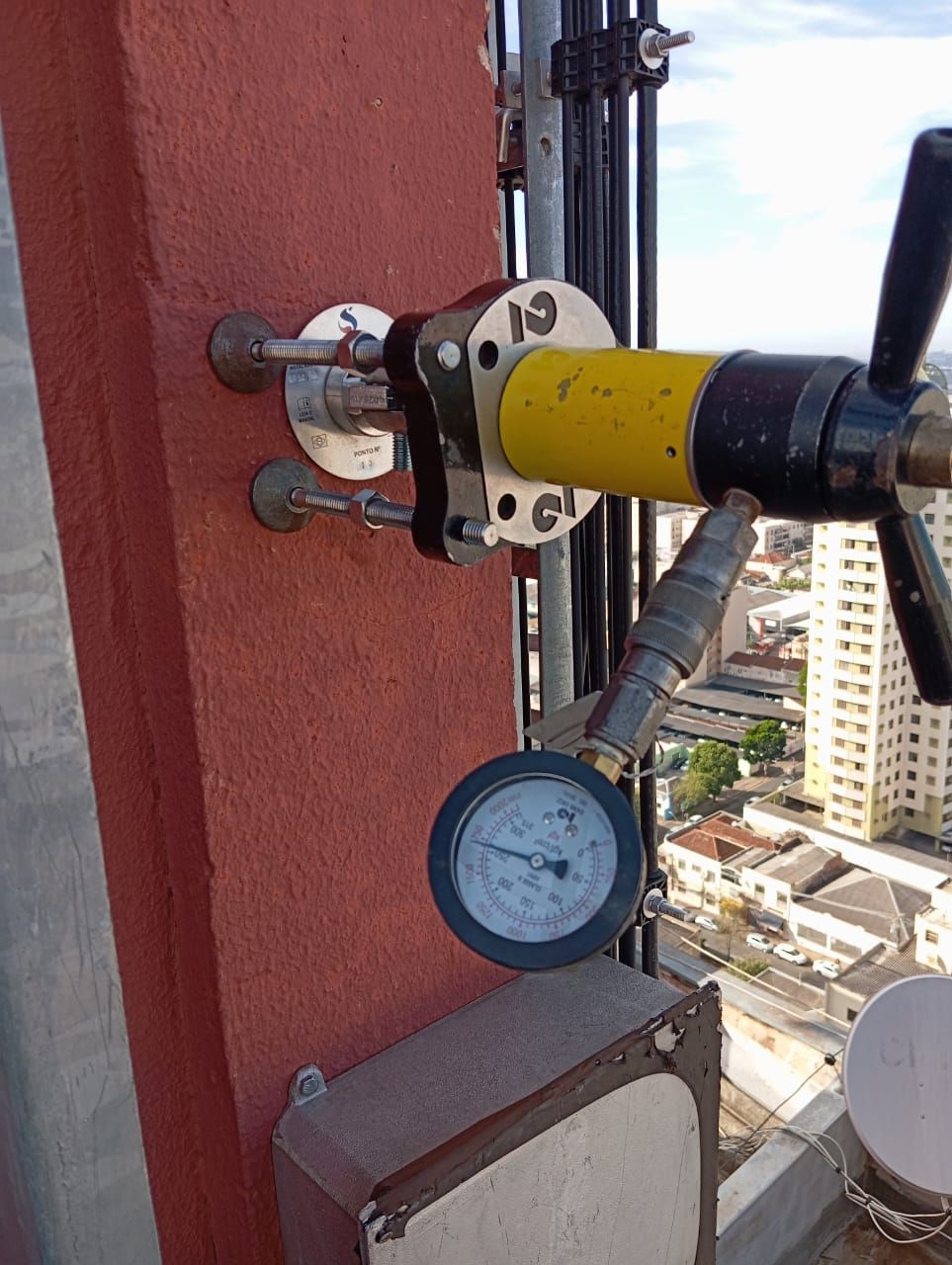 Teste de arranque em ponto de ancoragem definitivo, com manômetro, no alto de um edifício